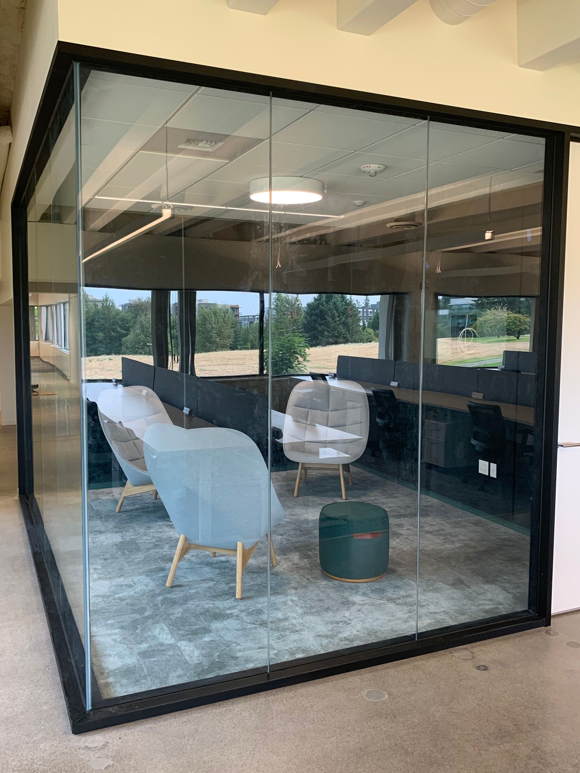 Glass-walled office space with seating: blue chairs, green ottoman, and a gray rug.
