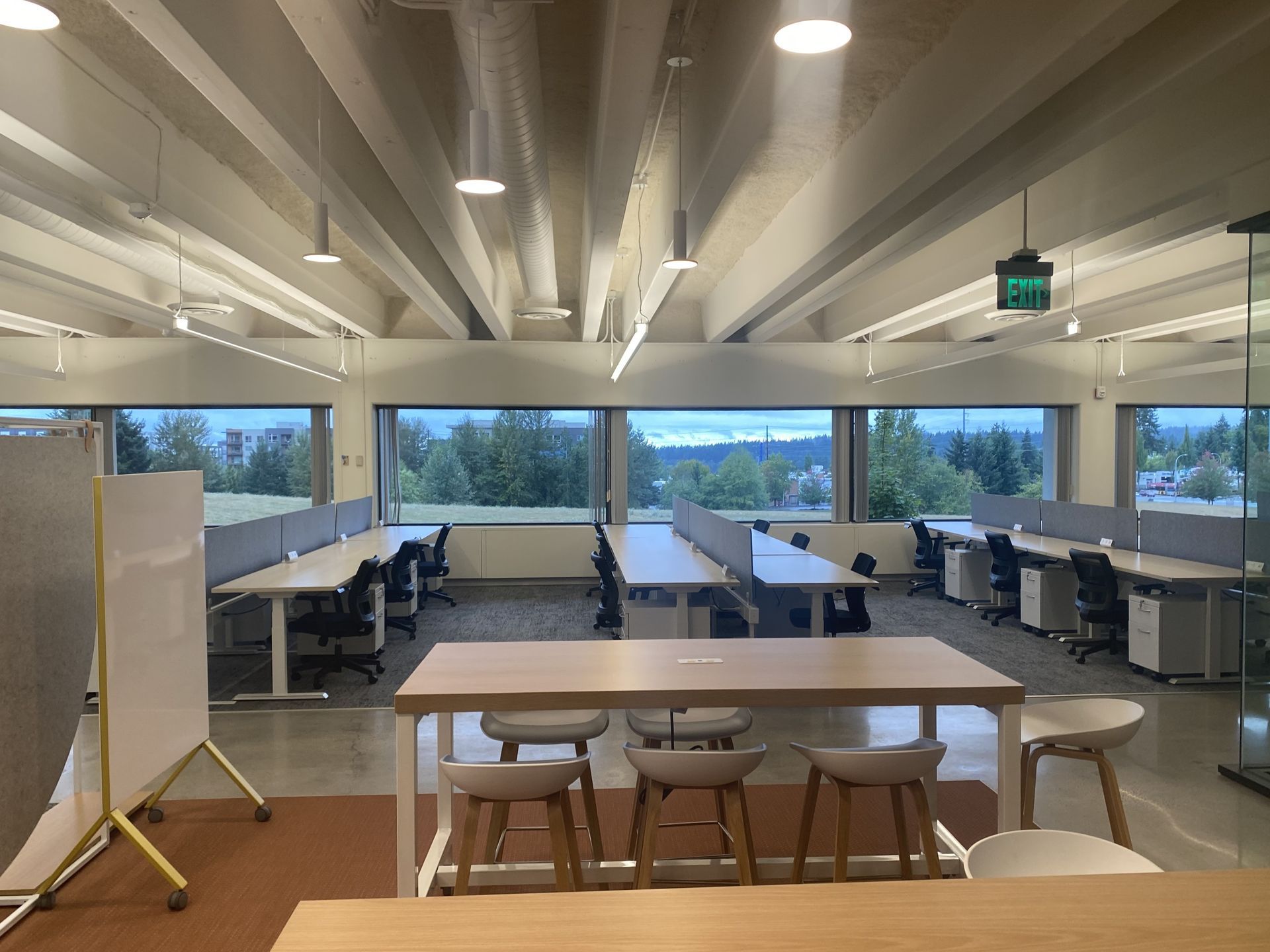 An office space with rows of desks, chairs, and large windows overlooking a green landscape.