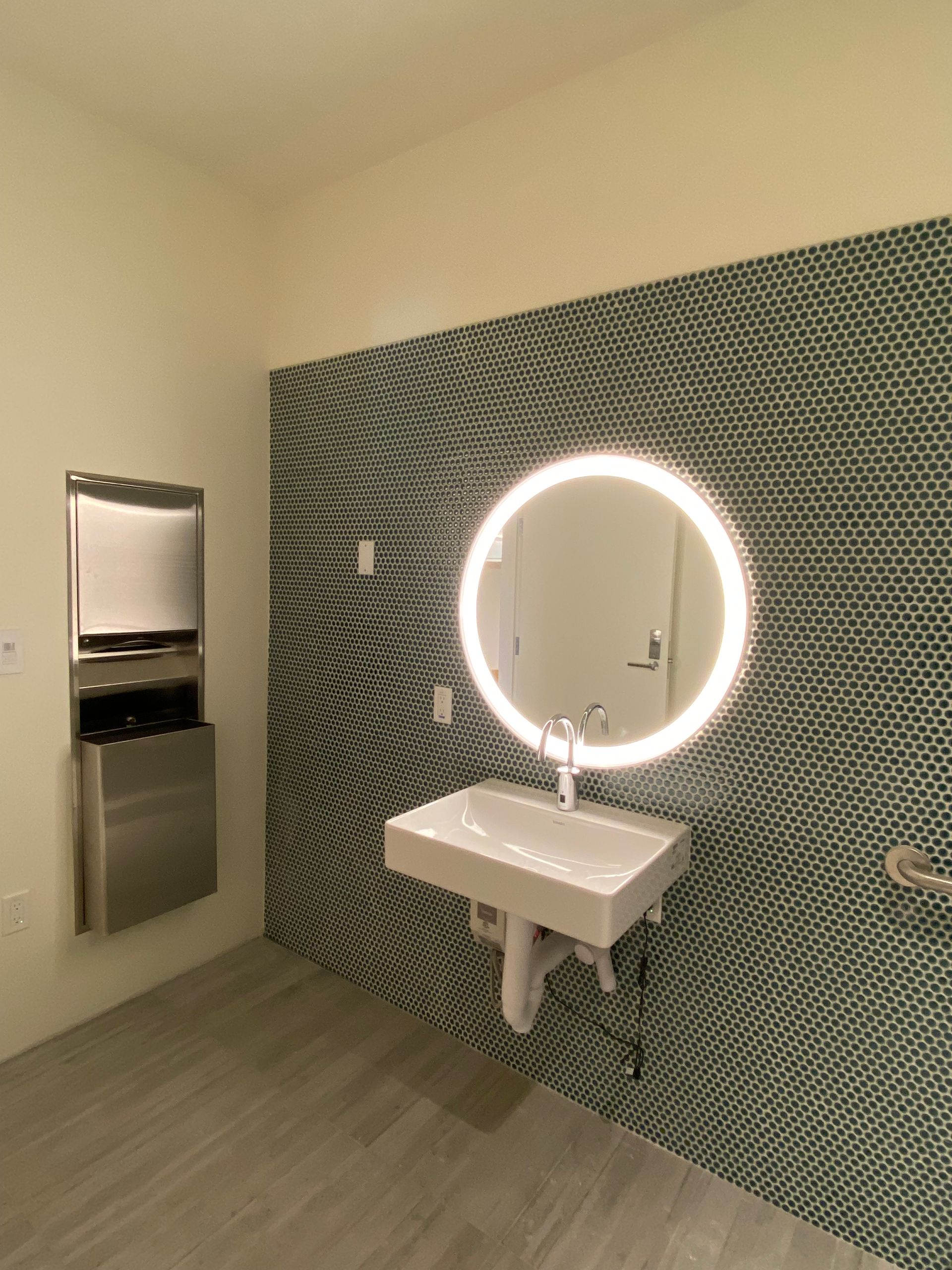 ADA-compliant public restroom with wall-mounted sink, mirror, and paper towel dispenser.