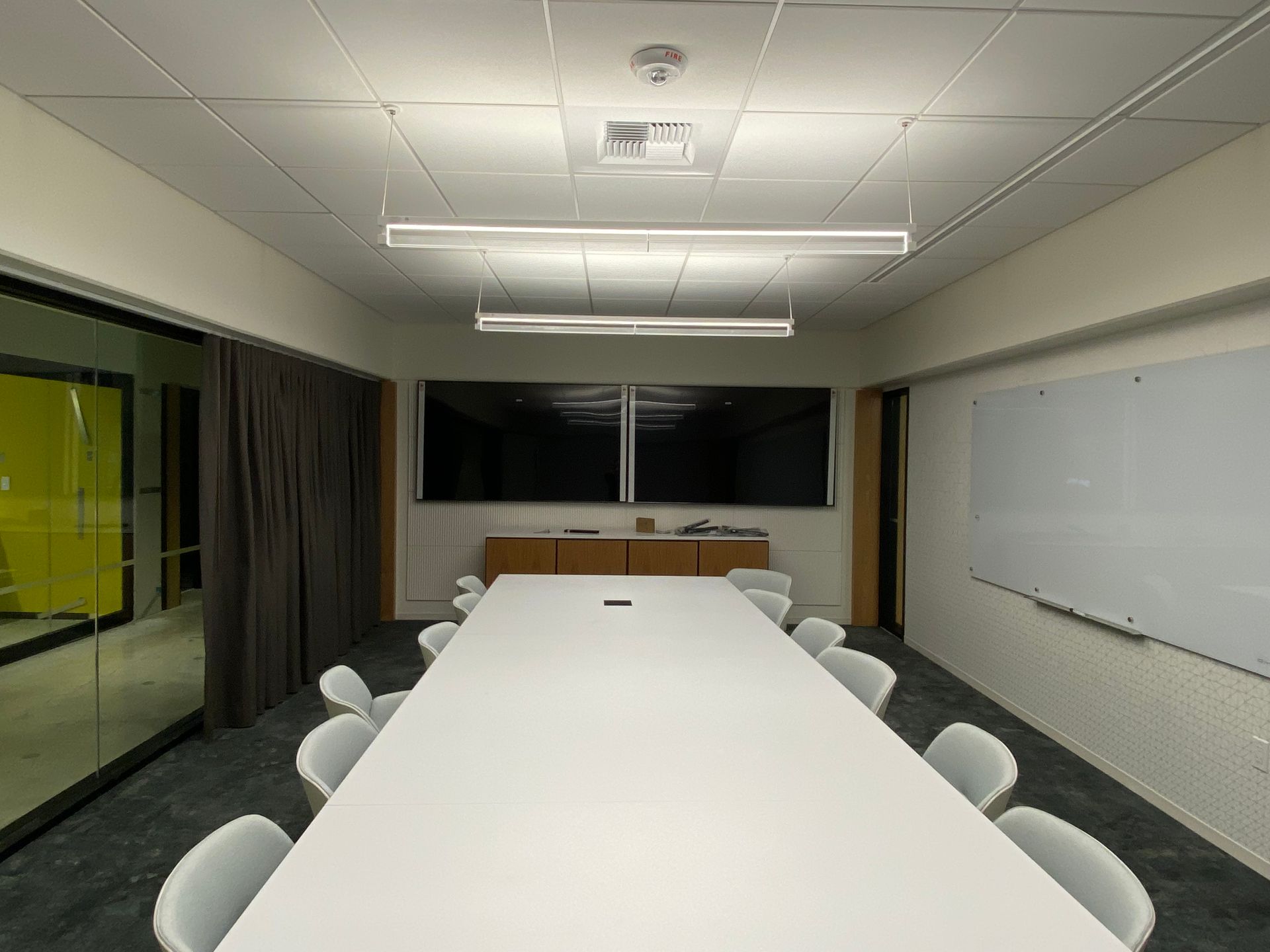 Conference room with a long white table, chairs, screens, and a whiteboard.