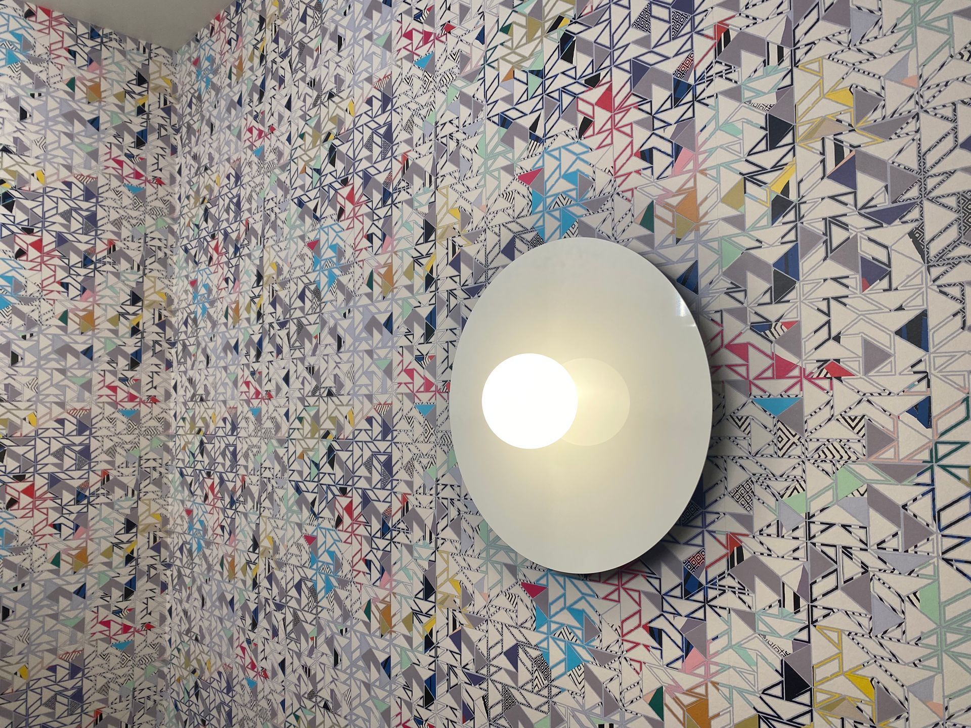 White wall light on a patterned wallpaper wall.