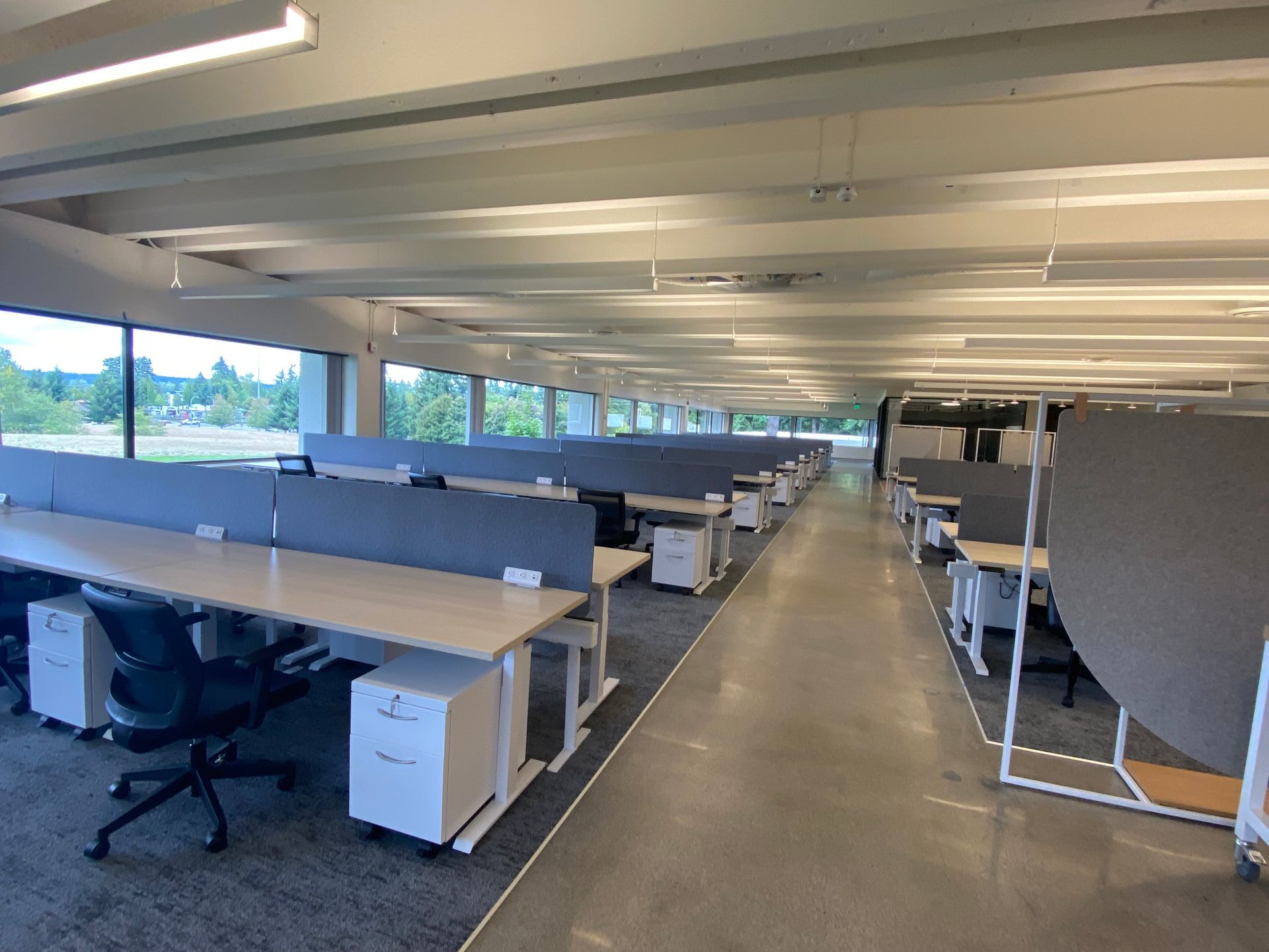 Empty modern office with rows of desks, windows along one side, and neutral colors.