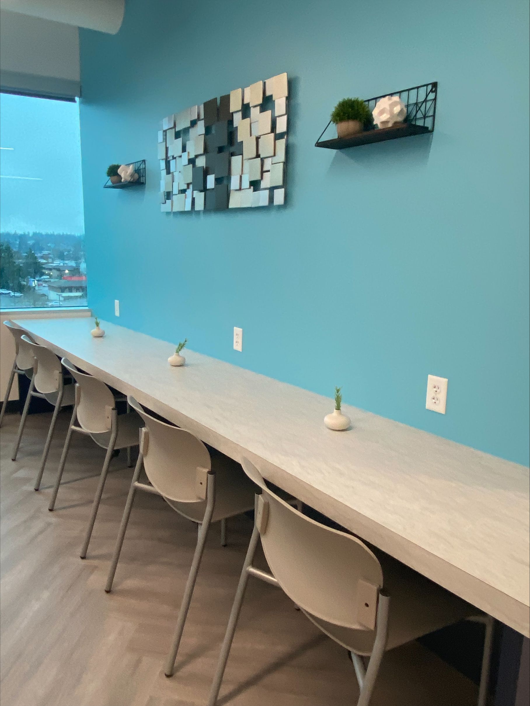 Long table with chairs along a blue wall. Artwork and shelves with decor are mounted above.