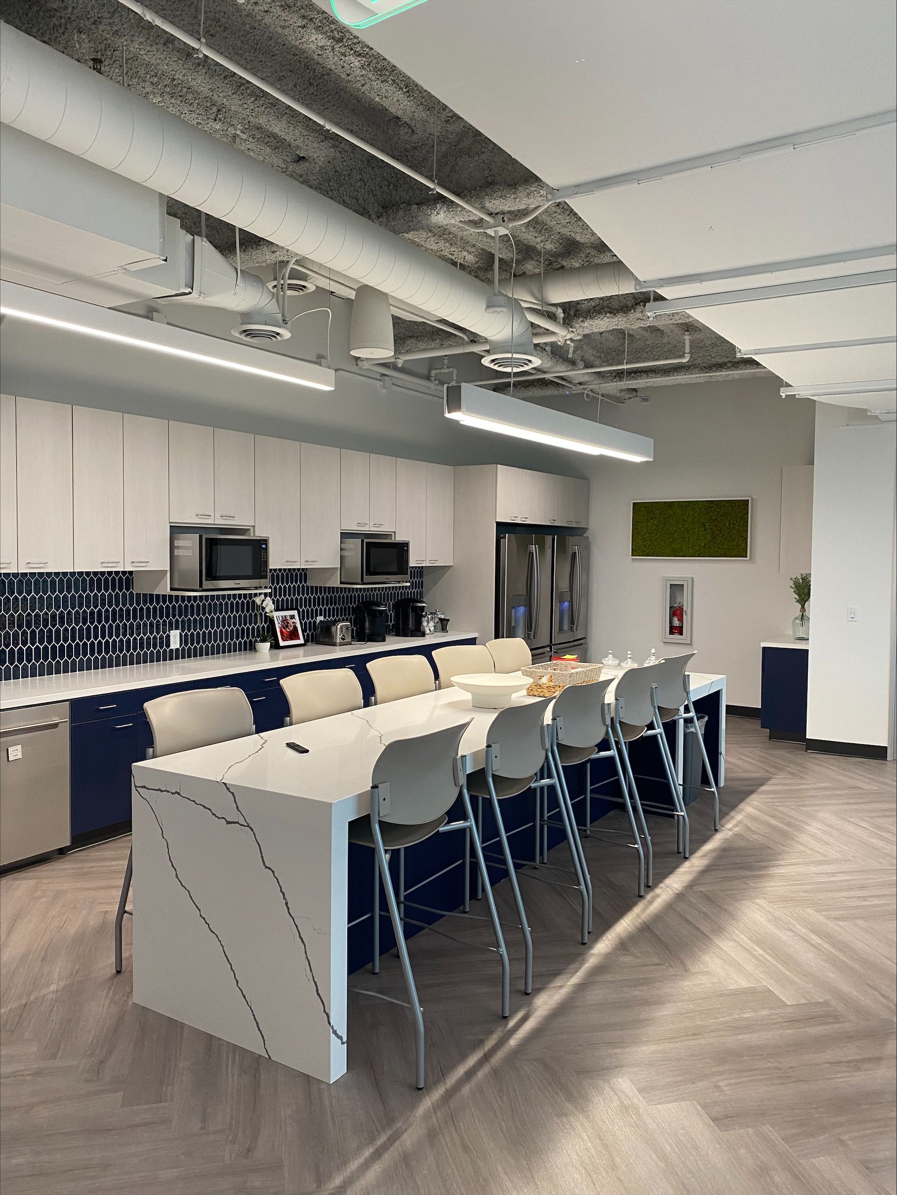 Modern office kitchen with long island seating, white cabinets, navy trim, stainless steel appliances.