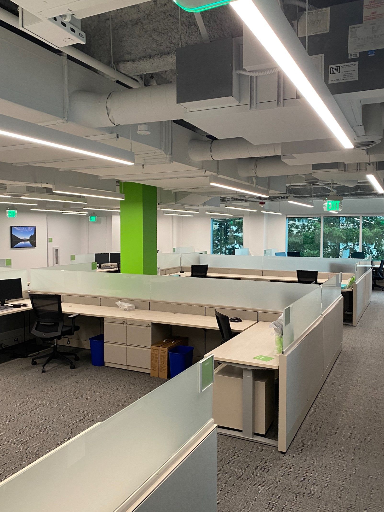 Modern office space with cubicles, white and green accents, and fluorescent lighting.