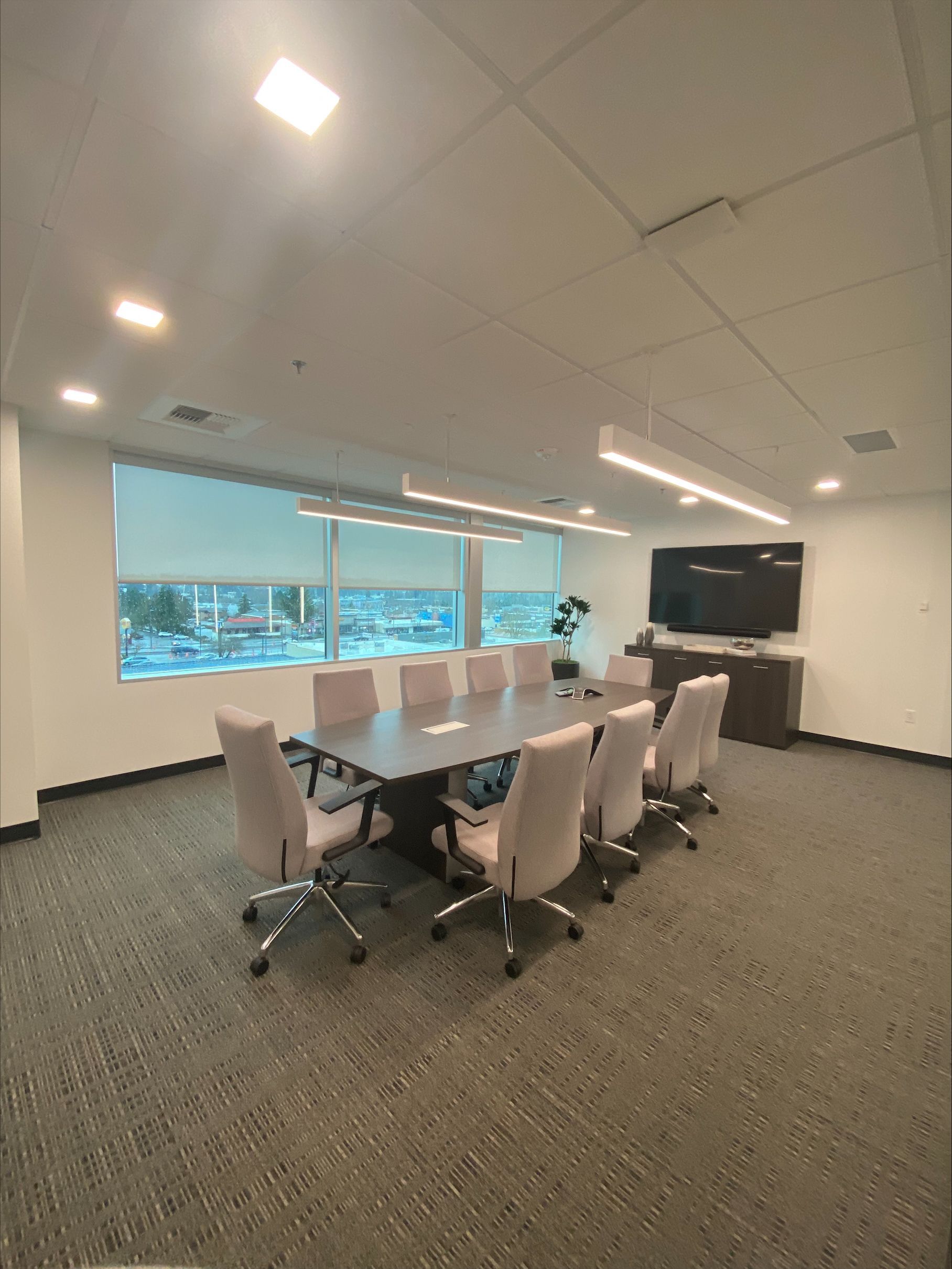 Conference room with dark table, light chairs, TV, window, and gray carpet.