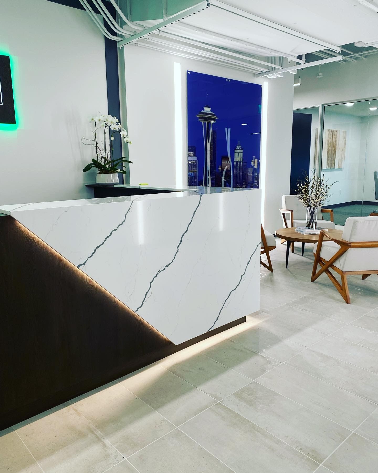 Modern office reception area with a white marble desk, a blue cityscape backdrop, and seating area.