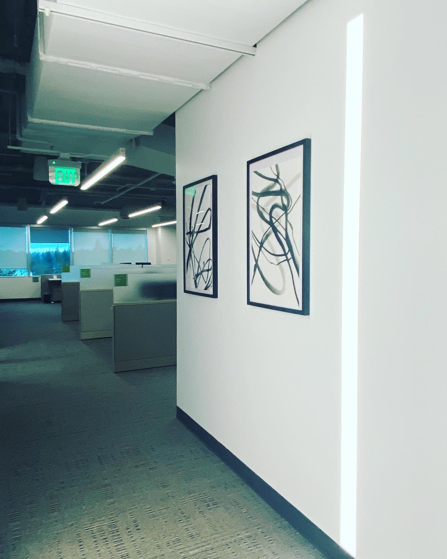 Office hallway with white walls, artwork, and cubicles.
