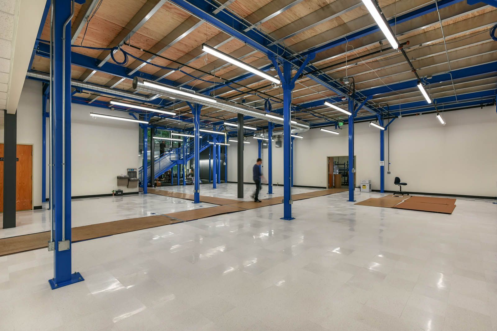 Interior view of a spacious room with blue beams, white walls, and a person walking.