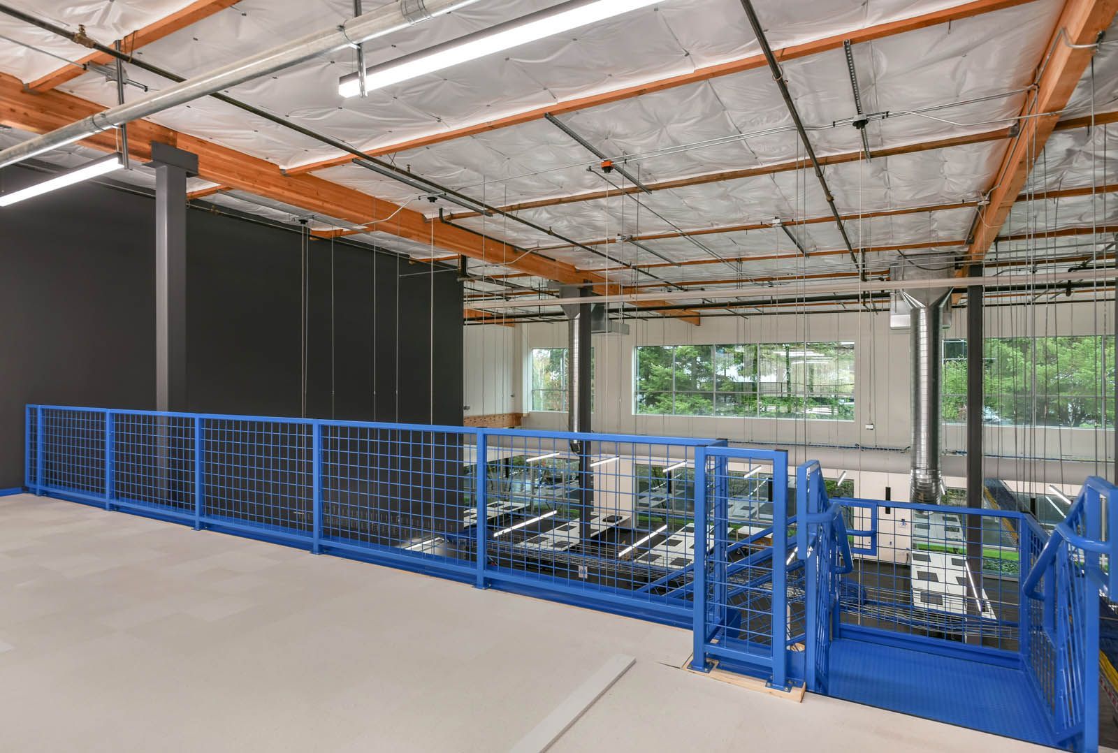 A blue metal platform in a modern open-concept space with exposed beams, pipes, and a black wall.