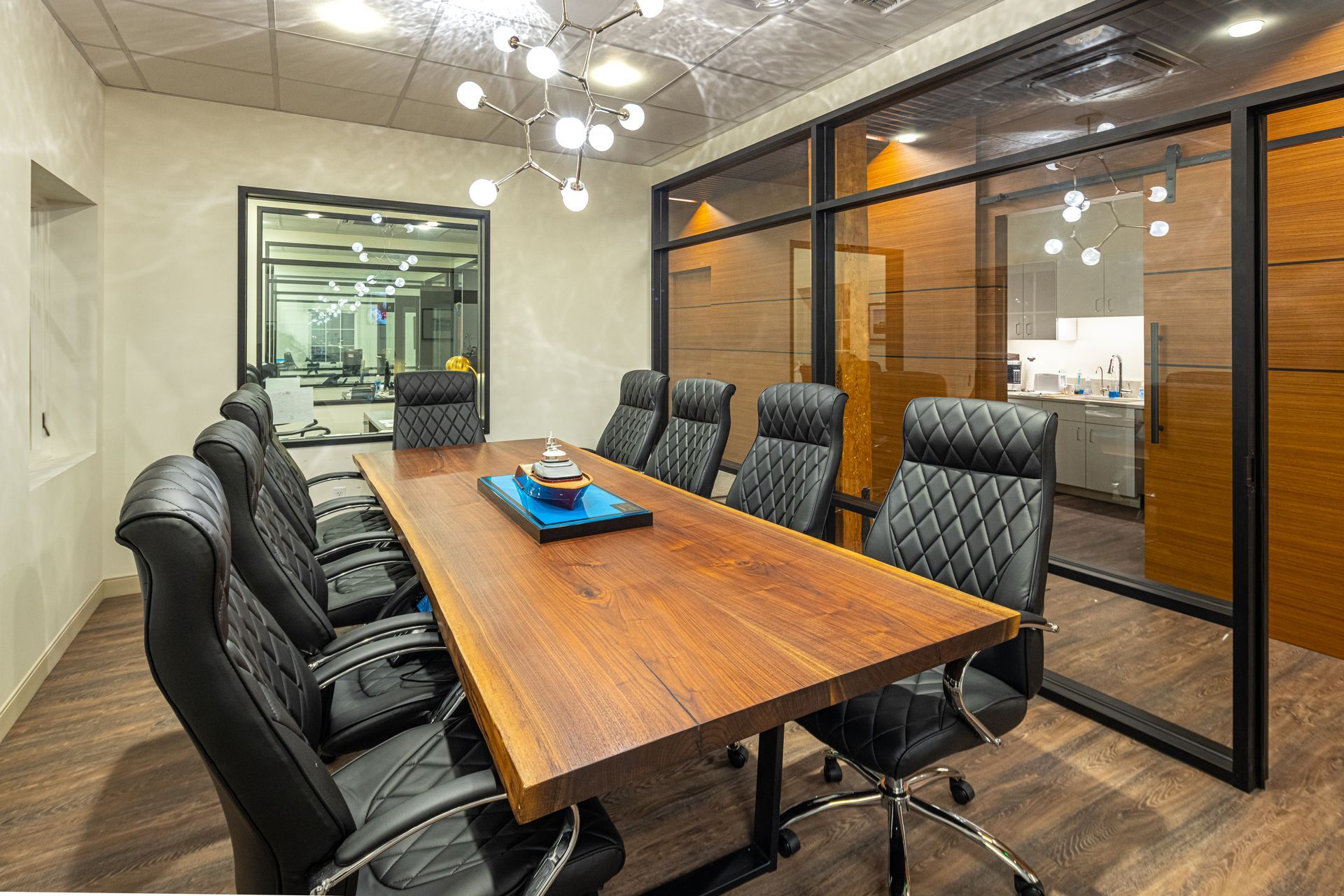 Conference room with long wooden table, black leather chairs, and glass walls.