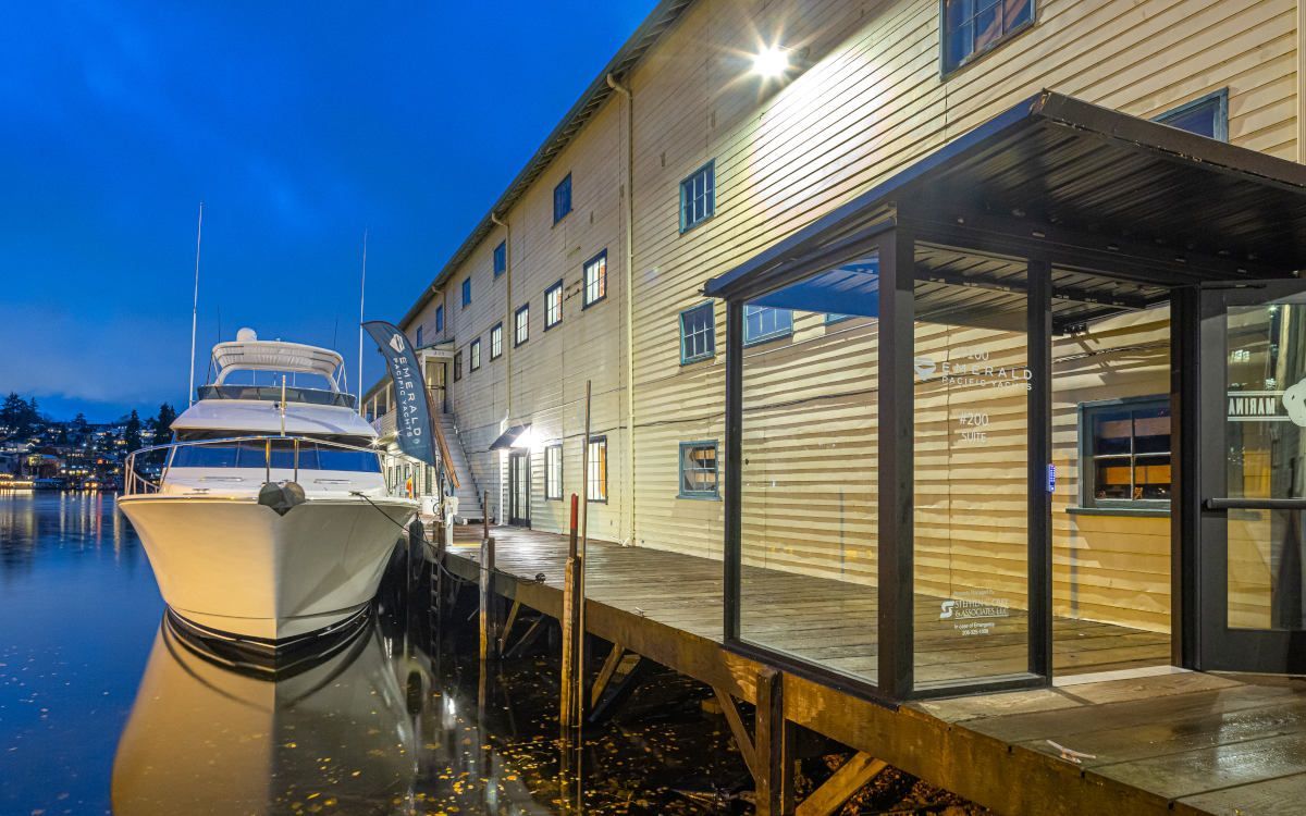 Boat docked at wooden pier next to a multi-story building at dusk; blue sky.