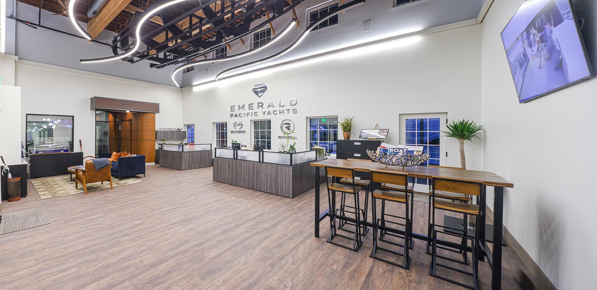 Interior of a business with a counter, seating, and a TV screen. The walls are white and the floors are a light brown color.