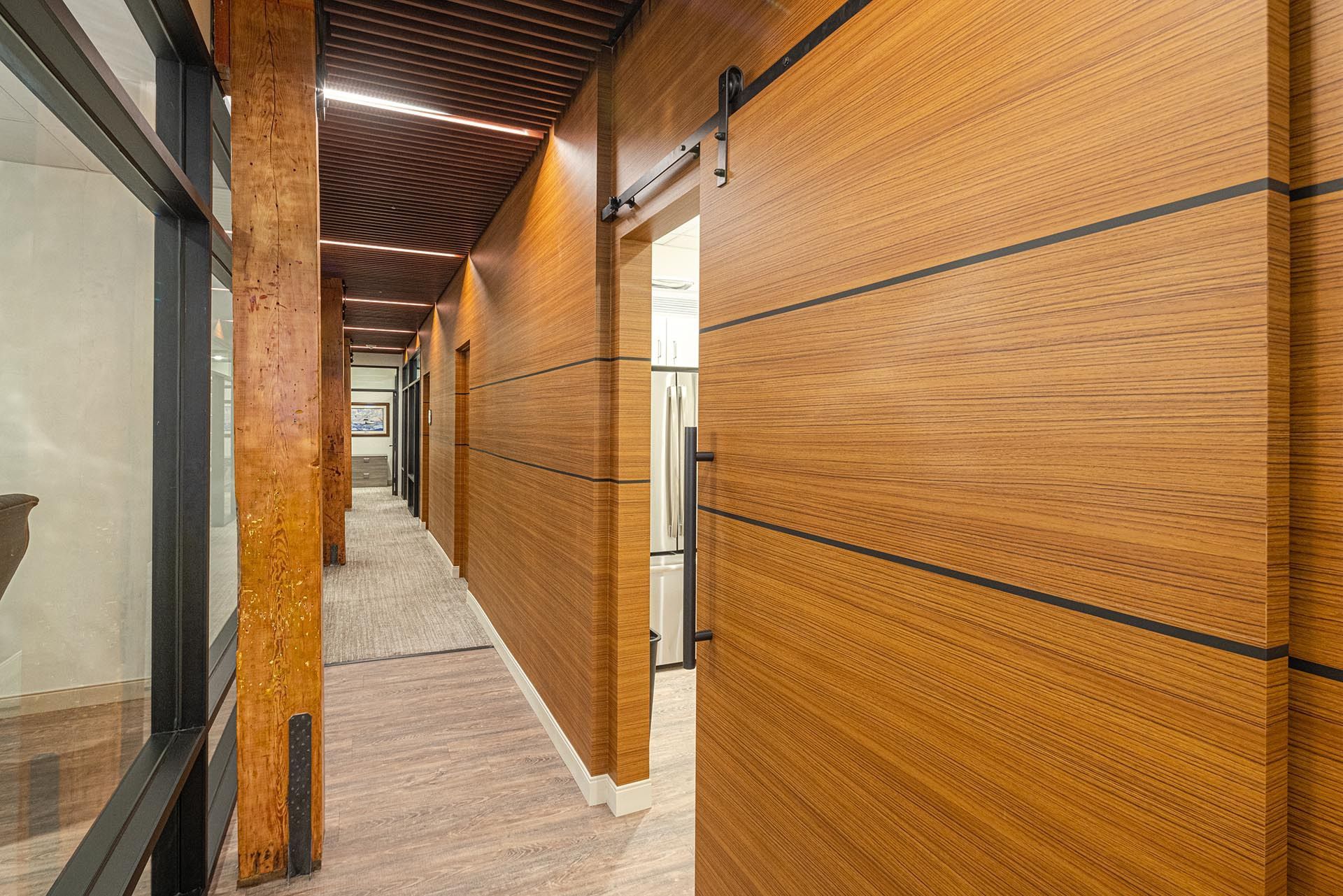 Long hallway with wood panel walls and doors, stone floor, and glass windows on the left.