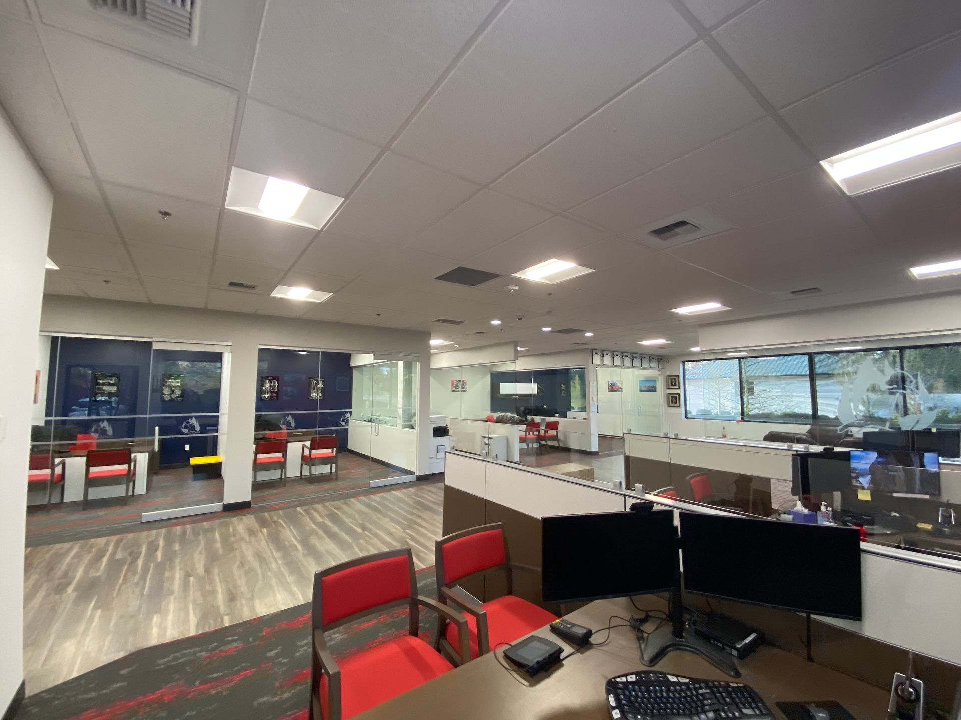 Interior office with workstations, red chairs, glass partitions, and multiple overhead lights.