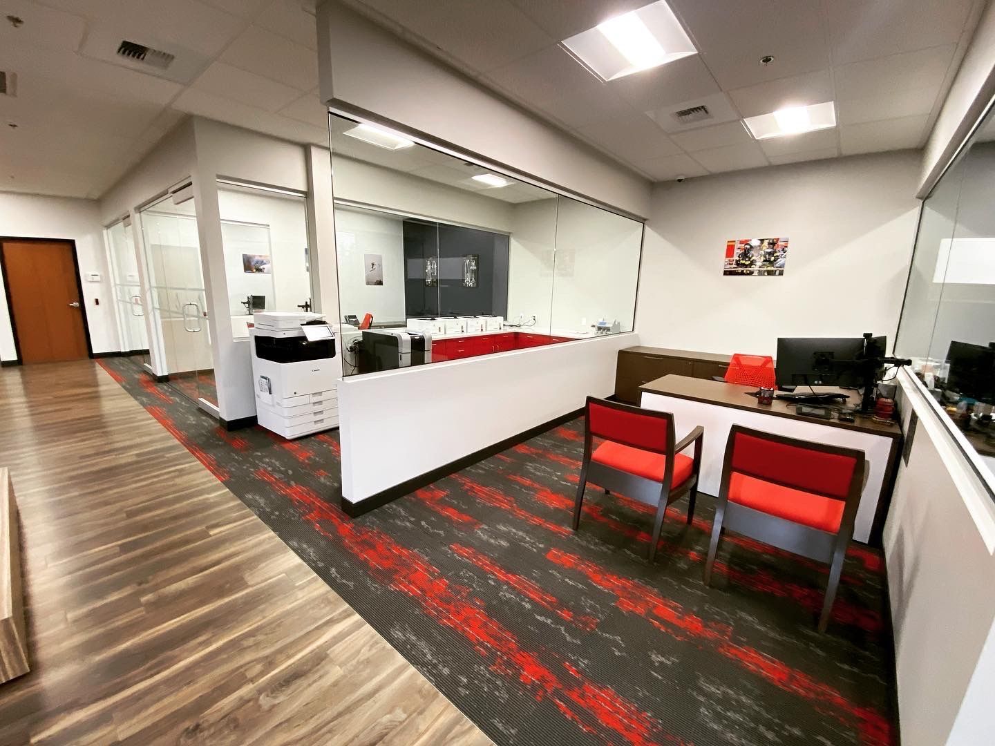 Office interior with red and black patterned carpet, white desks, and red chairs.