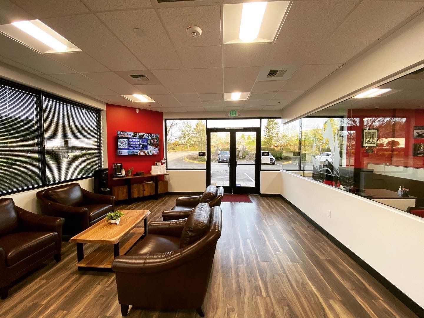 Waiting area with brown leather chairs, TV, wooden accents, and a glass door to the outside.