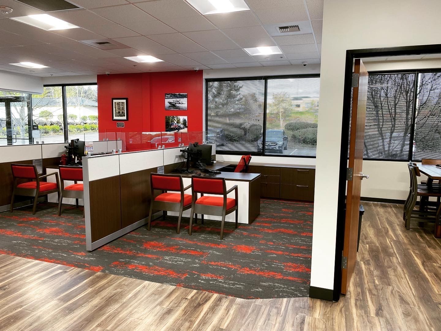 Office with red and brown cubicles, red chairs, and large windows with blinds.