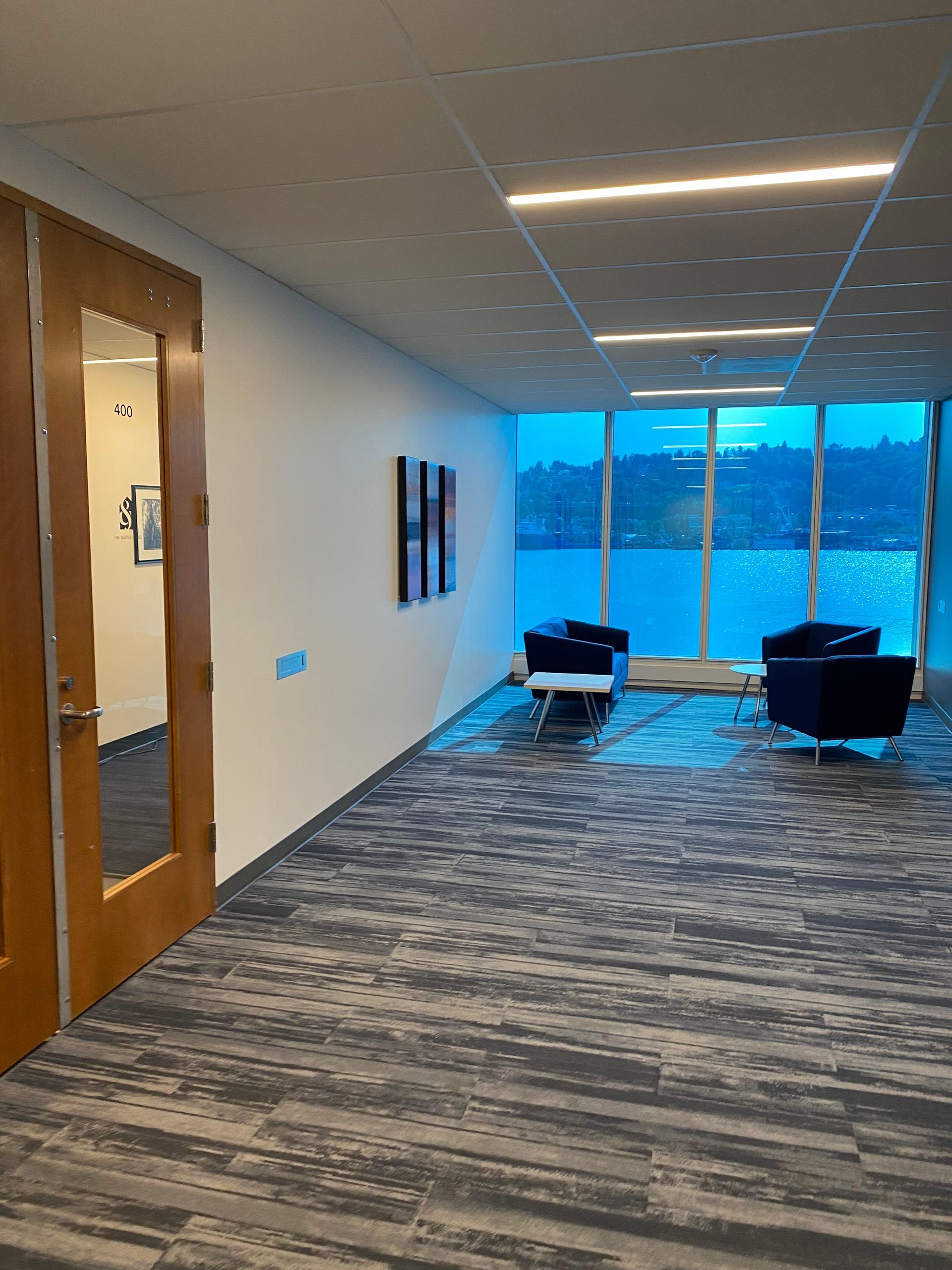 Corridor with blue water view, seating, art, and a closed door.