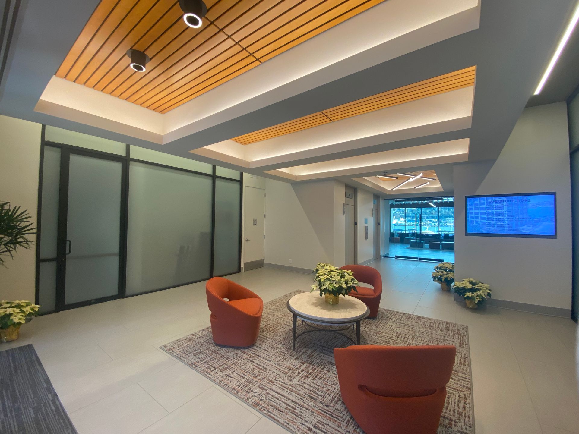 Lobby with orange chairs, coffee table, frosted glass doors, and a decorative ceiling with recessed lighting.