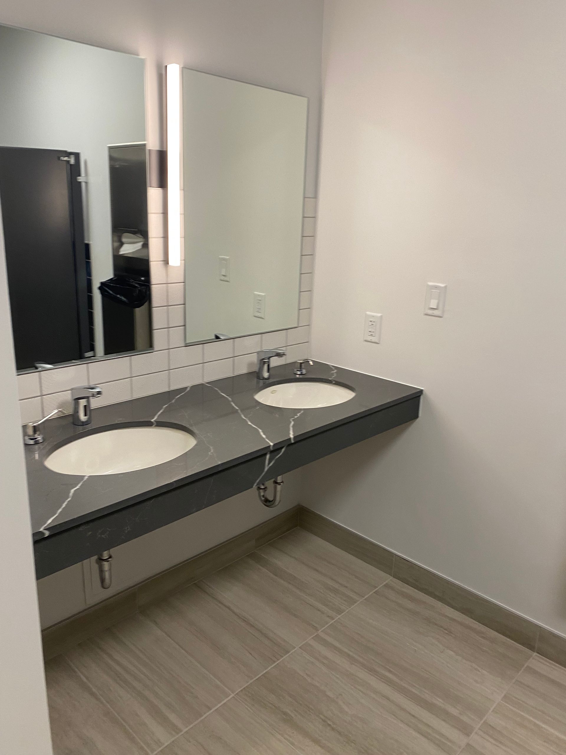 Modern bathroom with dual sinks and large mirrors, gray countertop, and light tile floor.