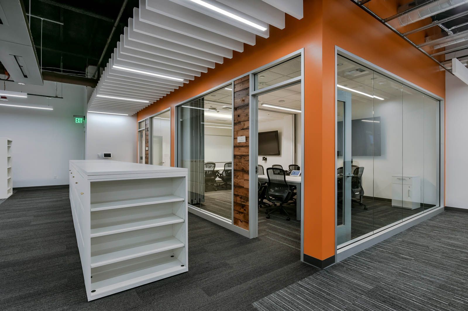 Modern office space with orange accents, glass walls, and a white bookshelf.