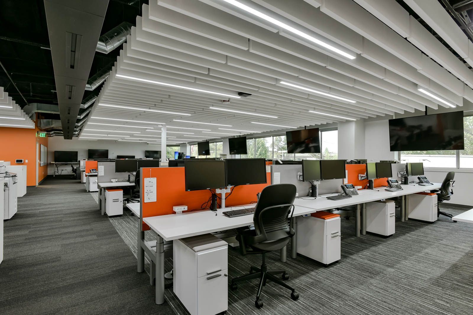 Modern office workspace with rows of desks, computer monitors, and orange dividers.
