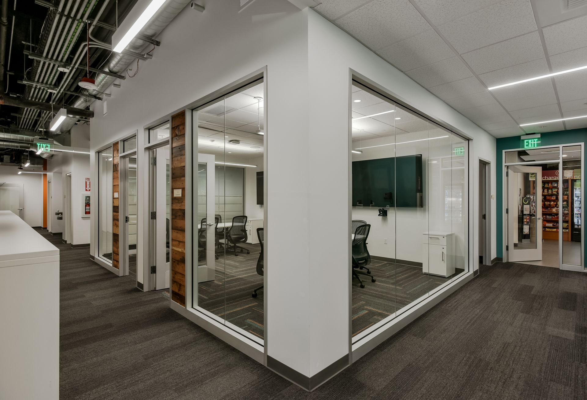 Office hallway with glass-walled conference rooms, dark carpet, and white walls.