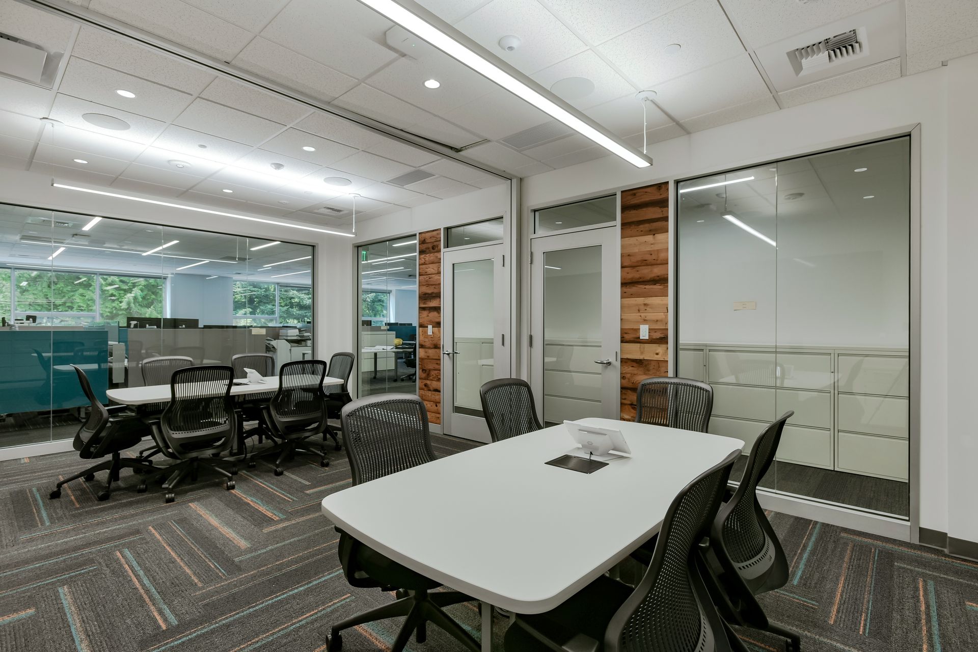 Modern office meeting room with white table, black chairs, and glass walls.