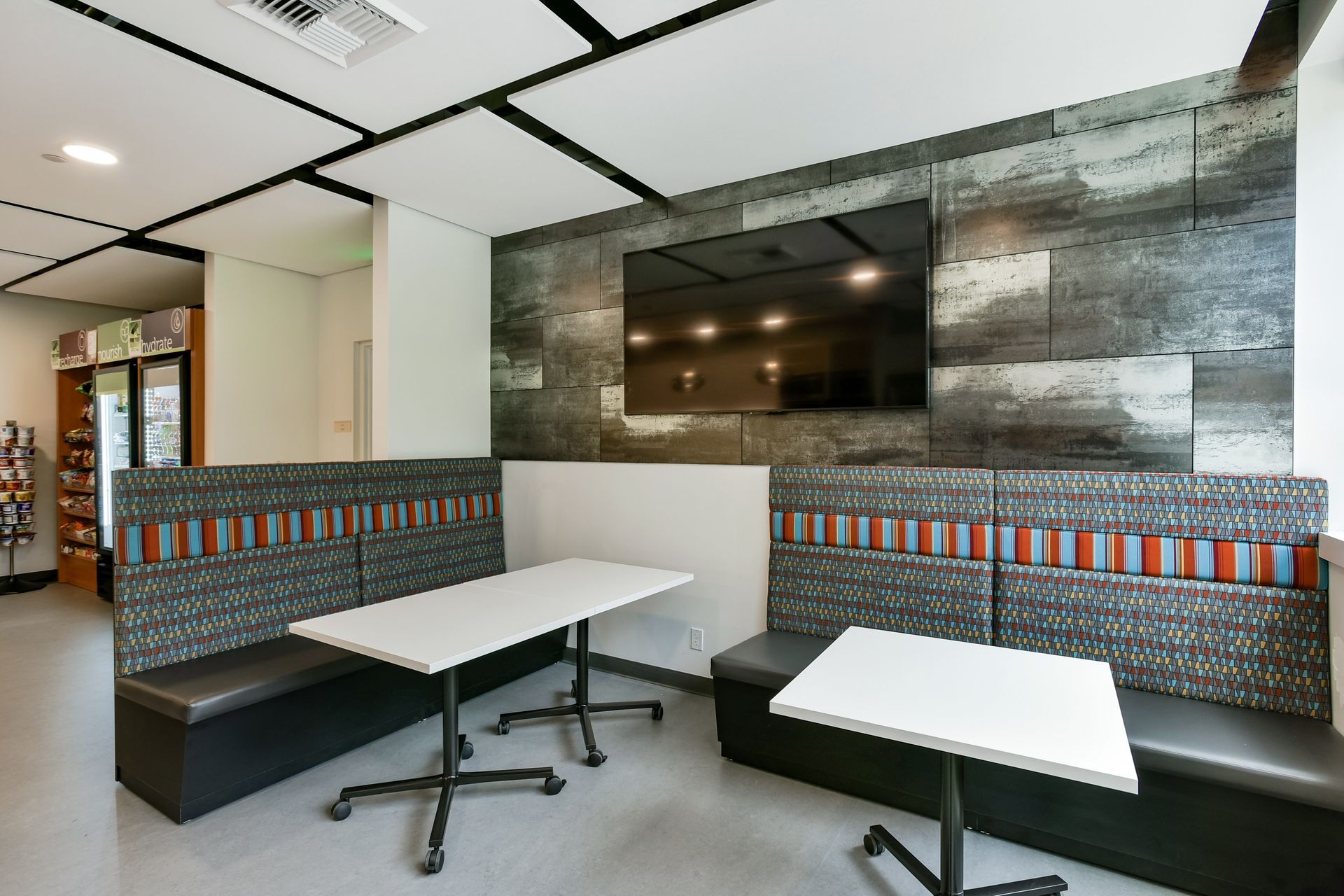 Booth seating with tables, a TV, and a vending machine in a modern lounge.