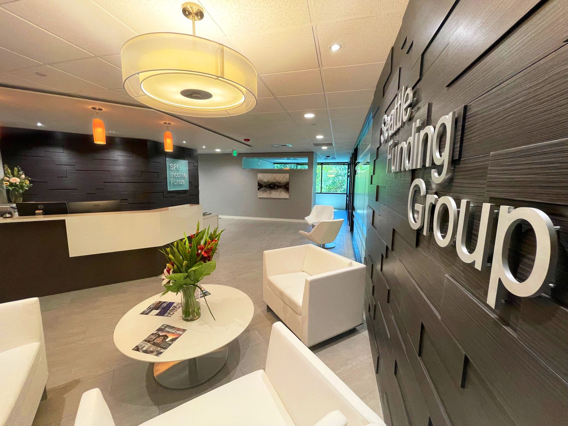 Modern office reception area with white furniture, wooden wall, and company signage.