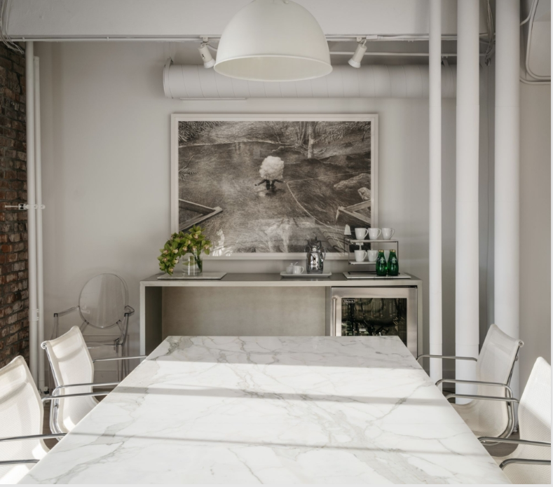 Modern meeting room with marble table, white chairs, and artwork. Drinks in mini-fridge.