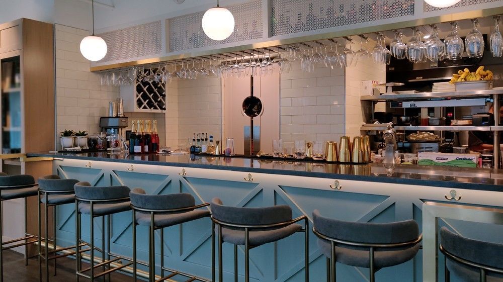Modern bar interior with blue stools, hanging pendant lights, and shelves of bottles behind the counter