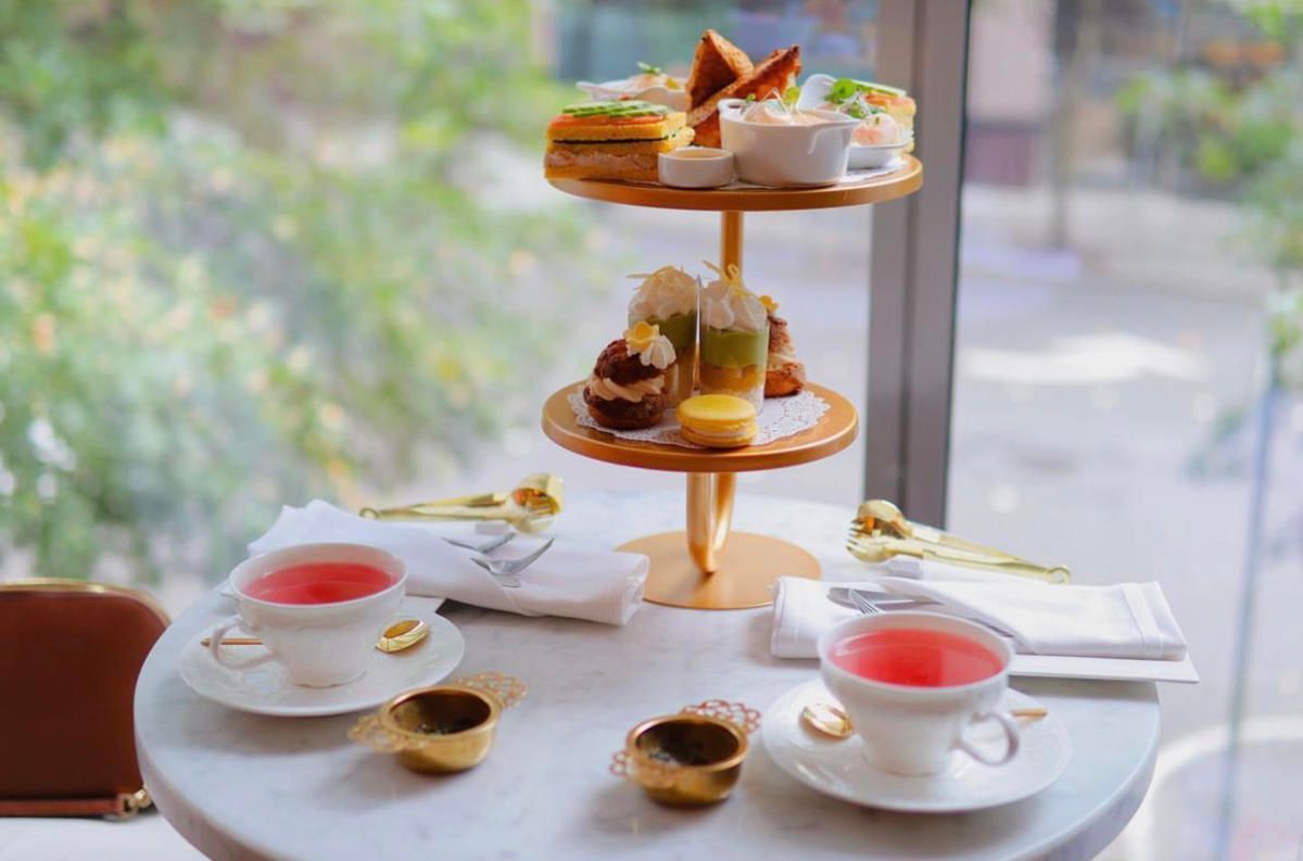 Afternoon tea table with tiered pastries, coffee cups, and plated desserts by a window