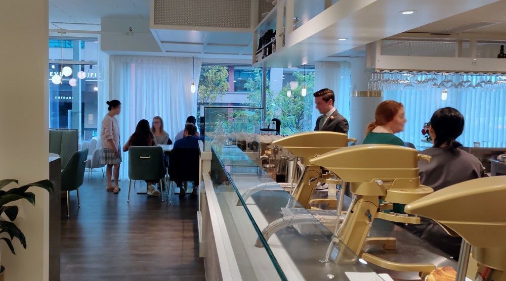 Modern café interior with people seated at tables beside a buffet counter and large windows