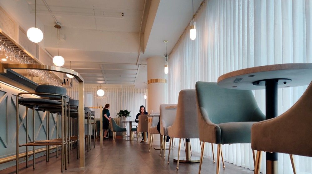 Modern café interior with wooden tables, chairs, pendant lights, and a few people in the background