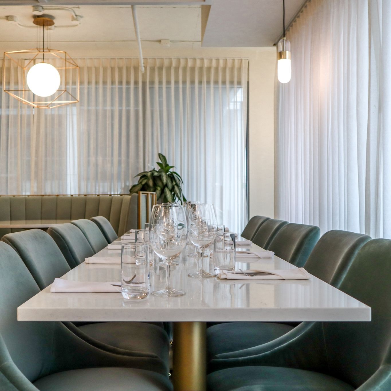 Modern dining room with a long white table, green upholstered chairs, and sheer curtains.