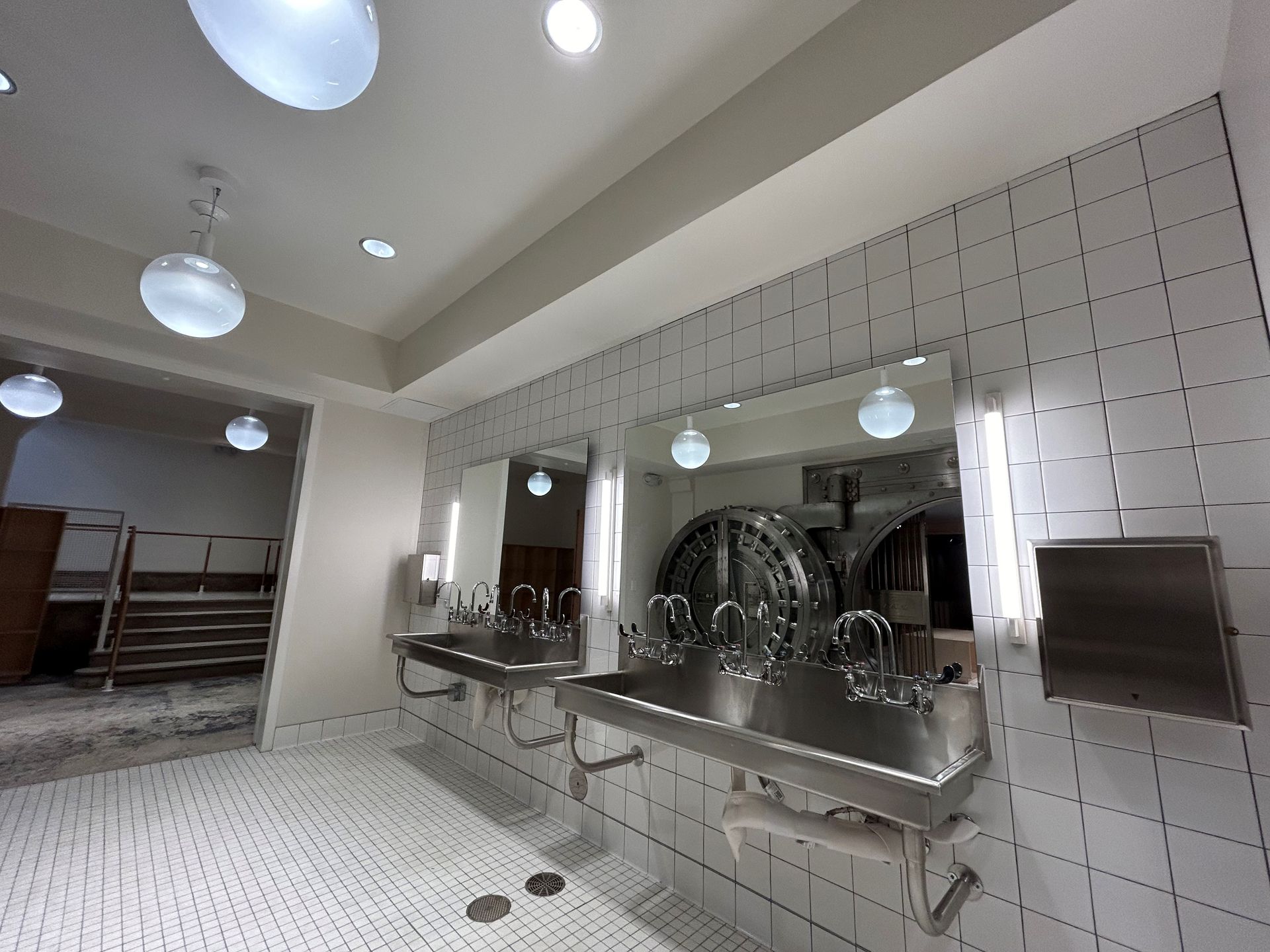 Public restroom with stainless steel sinks, mirrors, and white tiled walls.