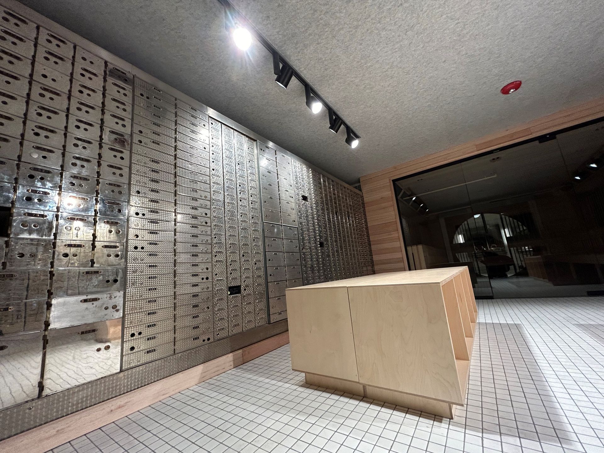 A room with mirrored wall of small doors, a light wooden table, and a tiled floor.