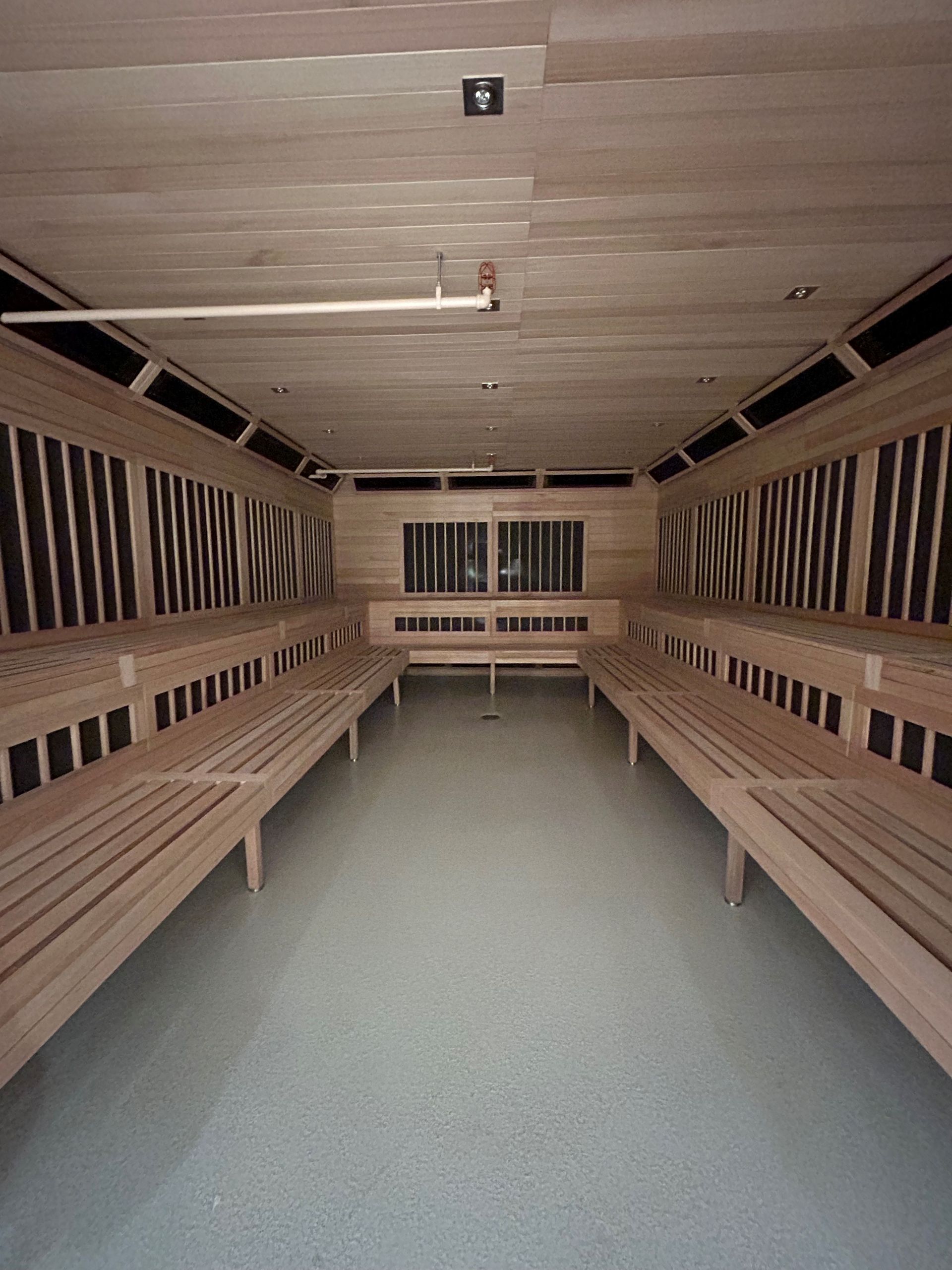 Interior view of a sauna with wooden benches, walls, and ceiling. Gray floor with a small drain.