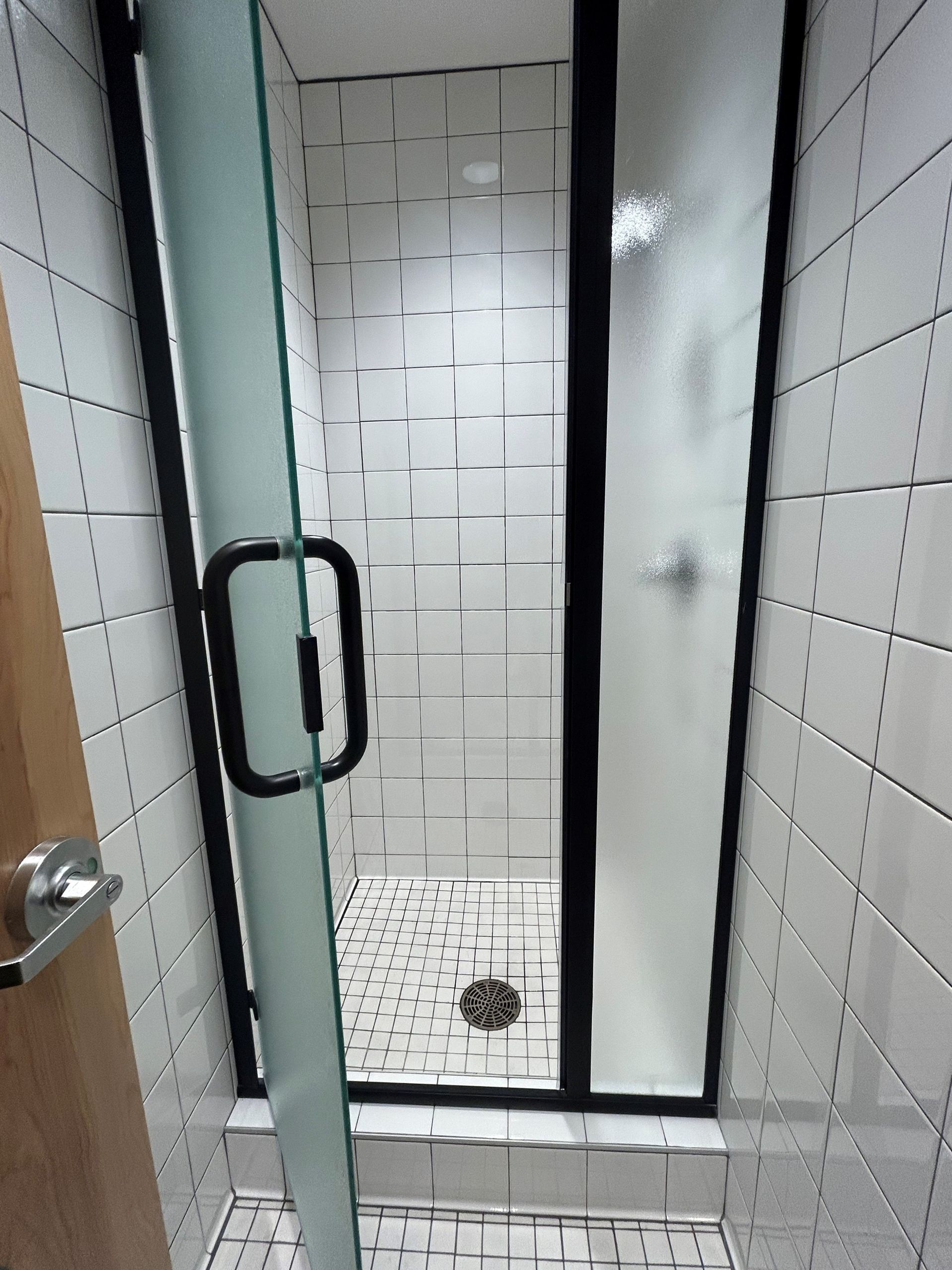 Shower stall with black frame, frosted glass door, white tiled walls.