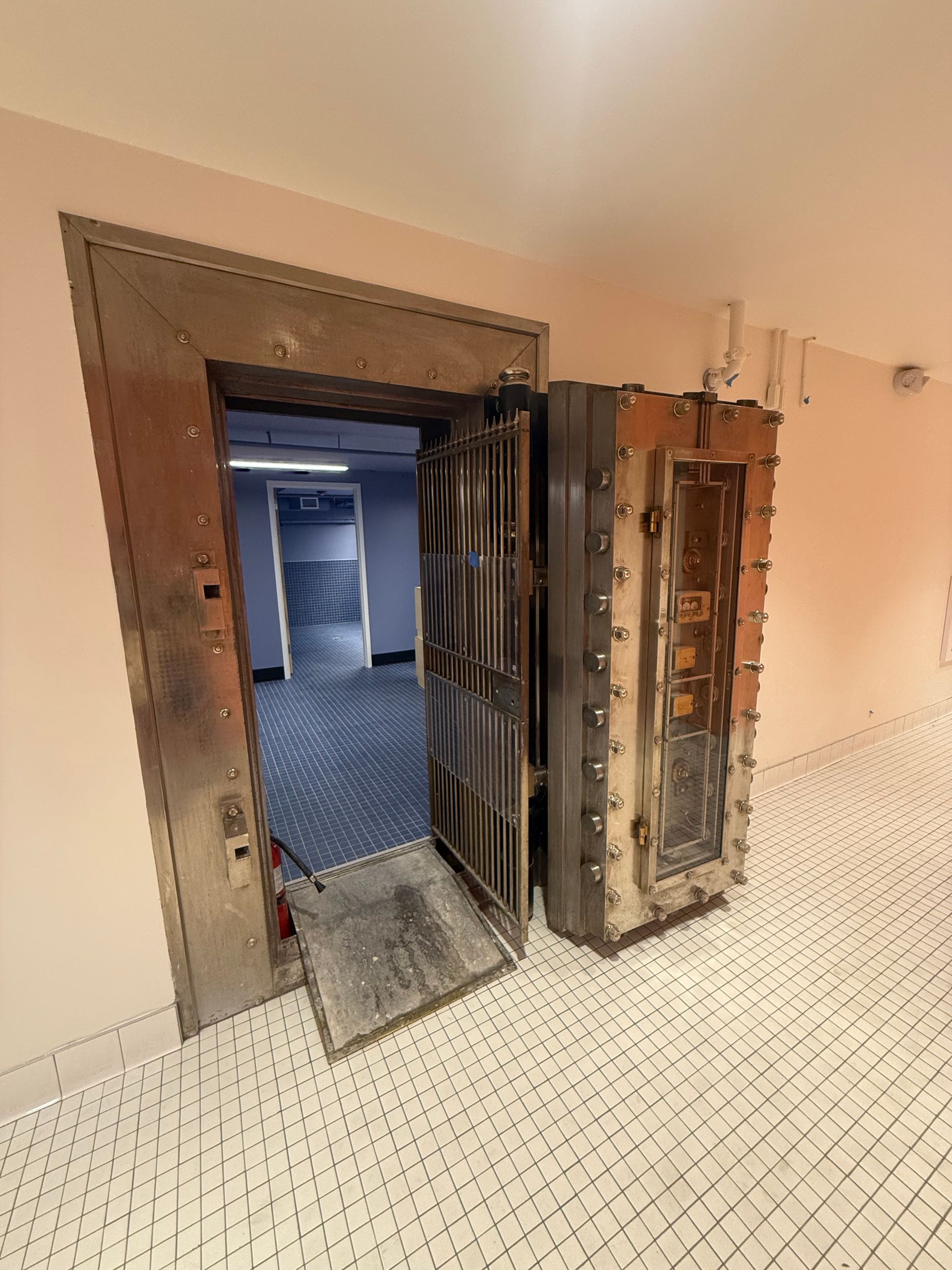 Open bank vault door in a hallway, revealing a room with blue carpet.