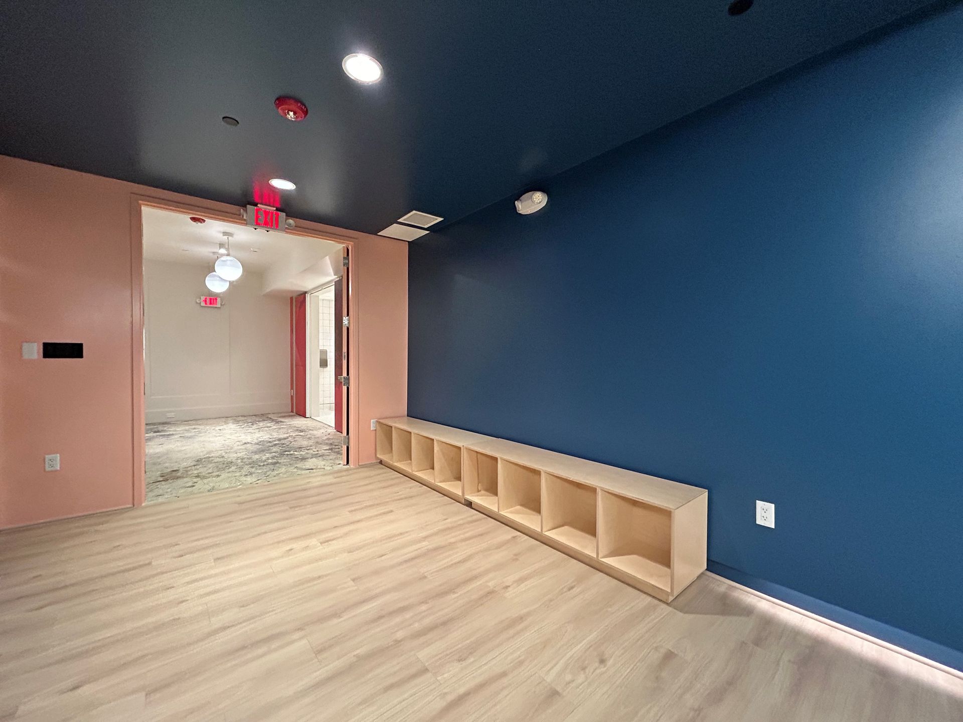 Empty room with blue and pink walls, light wood-look floor, and built-in cubbies.