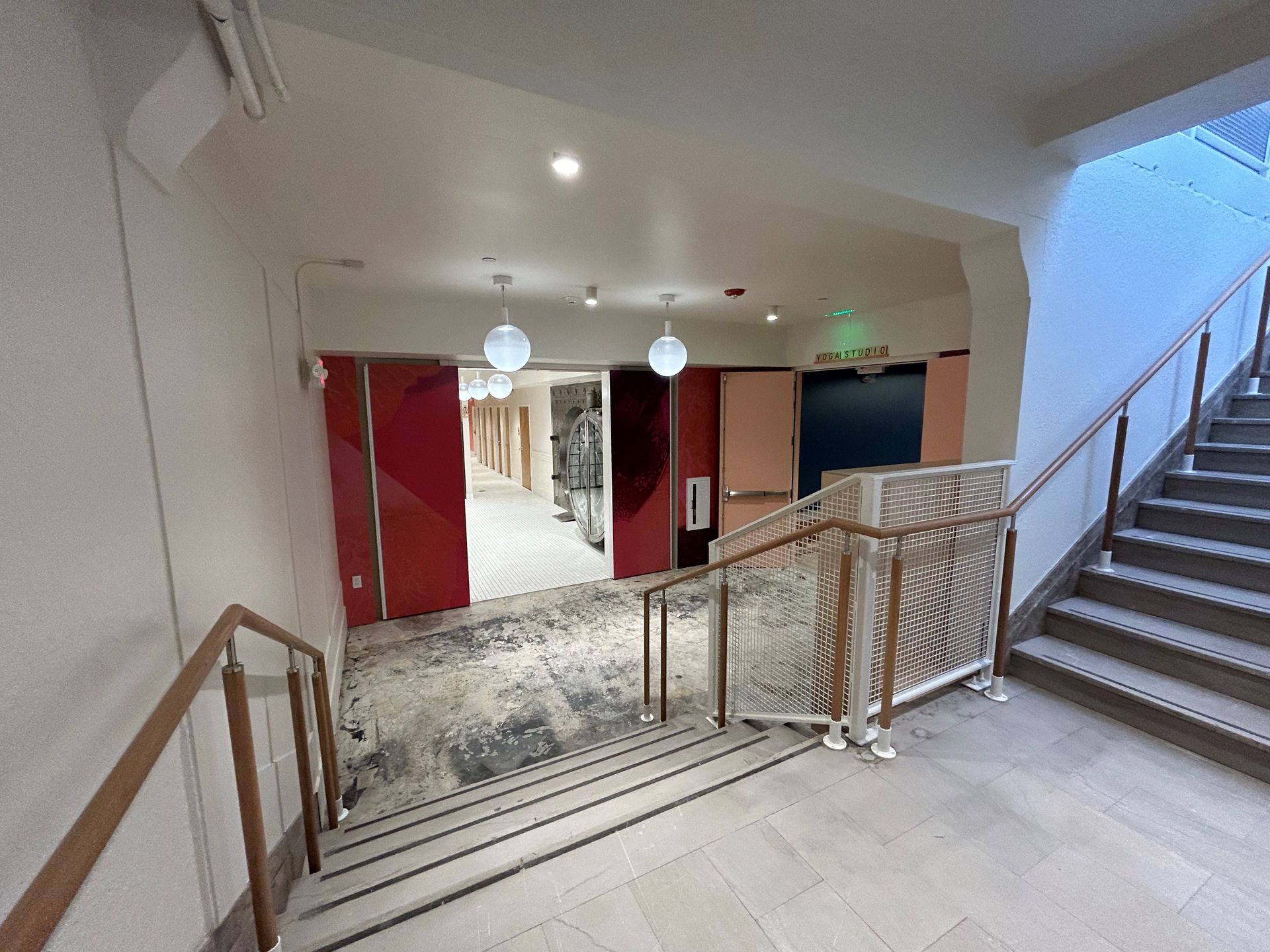 Stairway leads to a hallway with red doors and globe lights. A staircase is on the right.