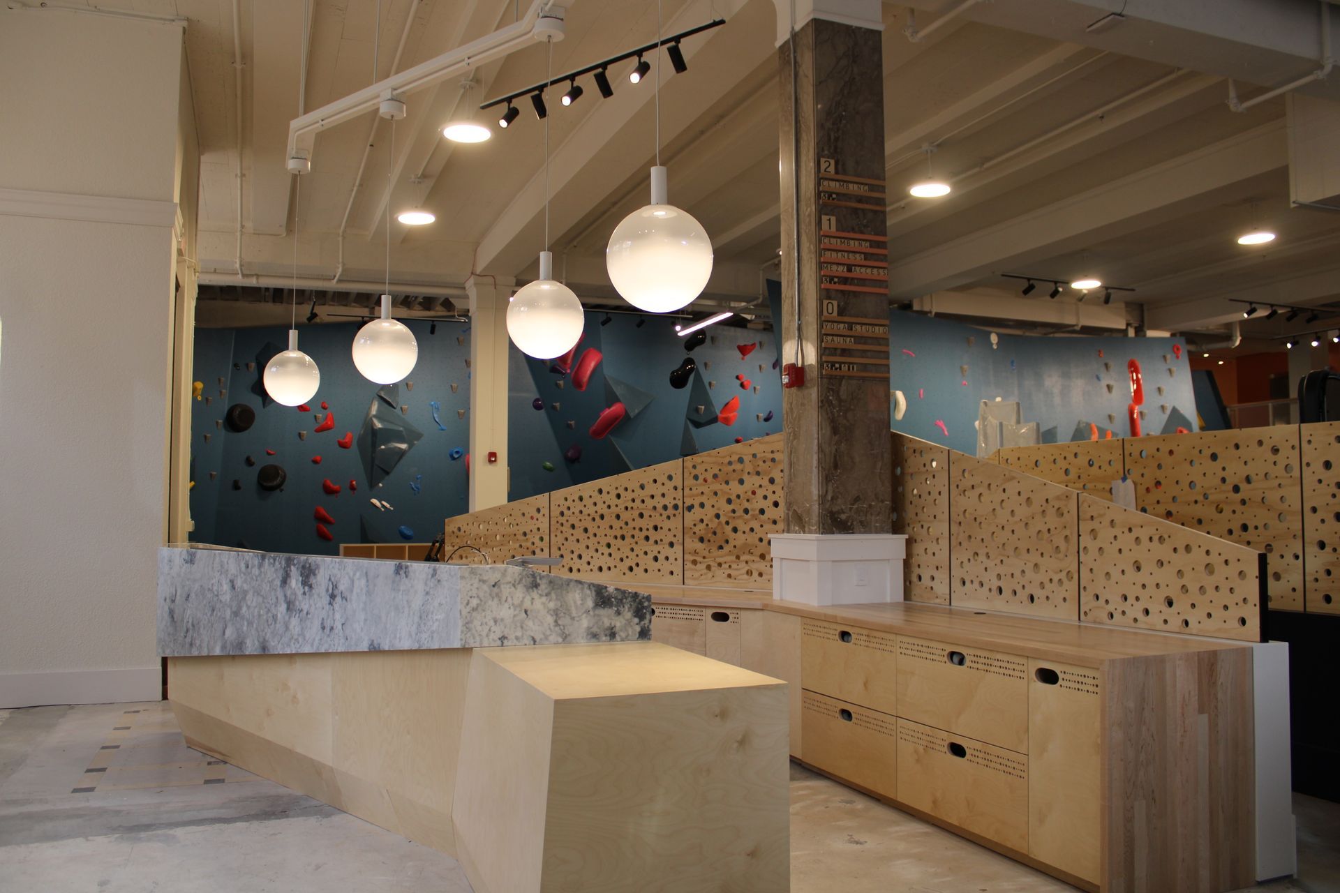 Interior of a climbing gym with climbing walls, wooden structures, and globe pendant lights.