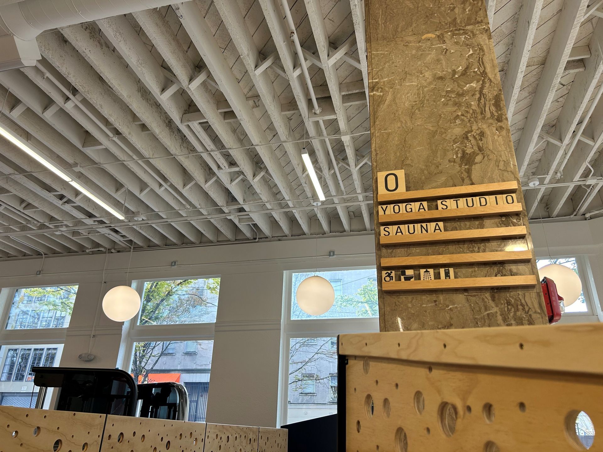 Sign on a concrete pillar in a cafe with a white grid ceiling, windows, and round lights.