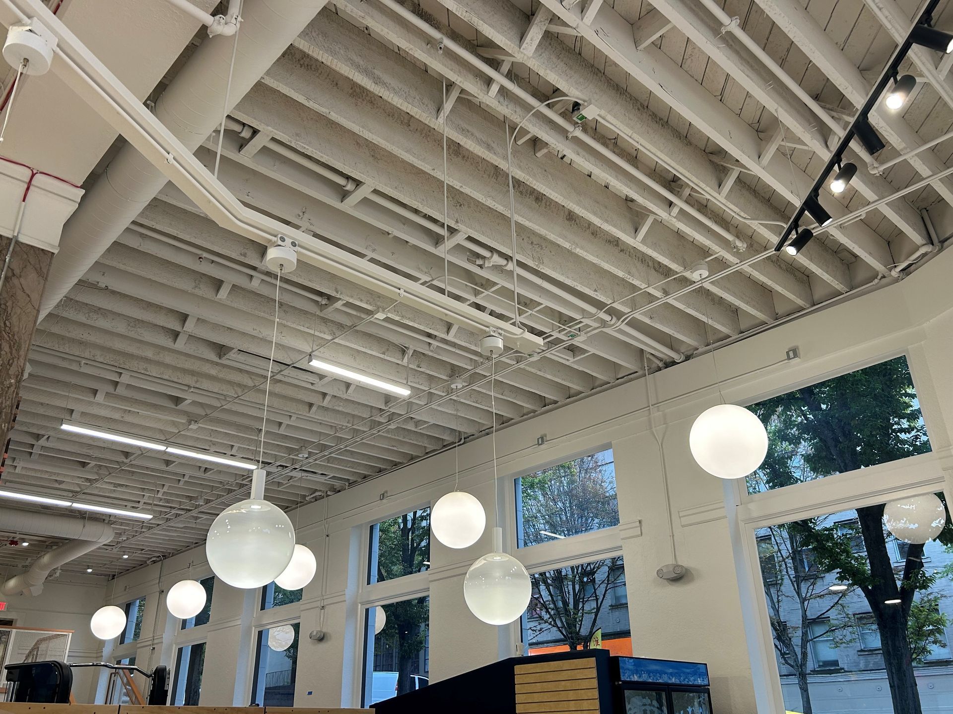 White ceiling with exposed beams, round pendant lights, and large windows.