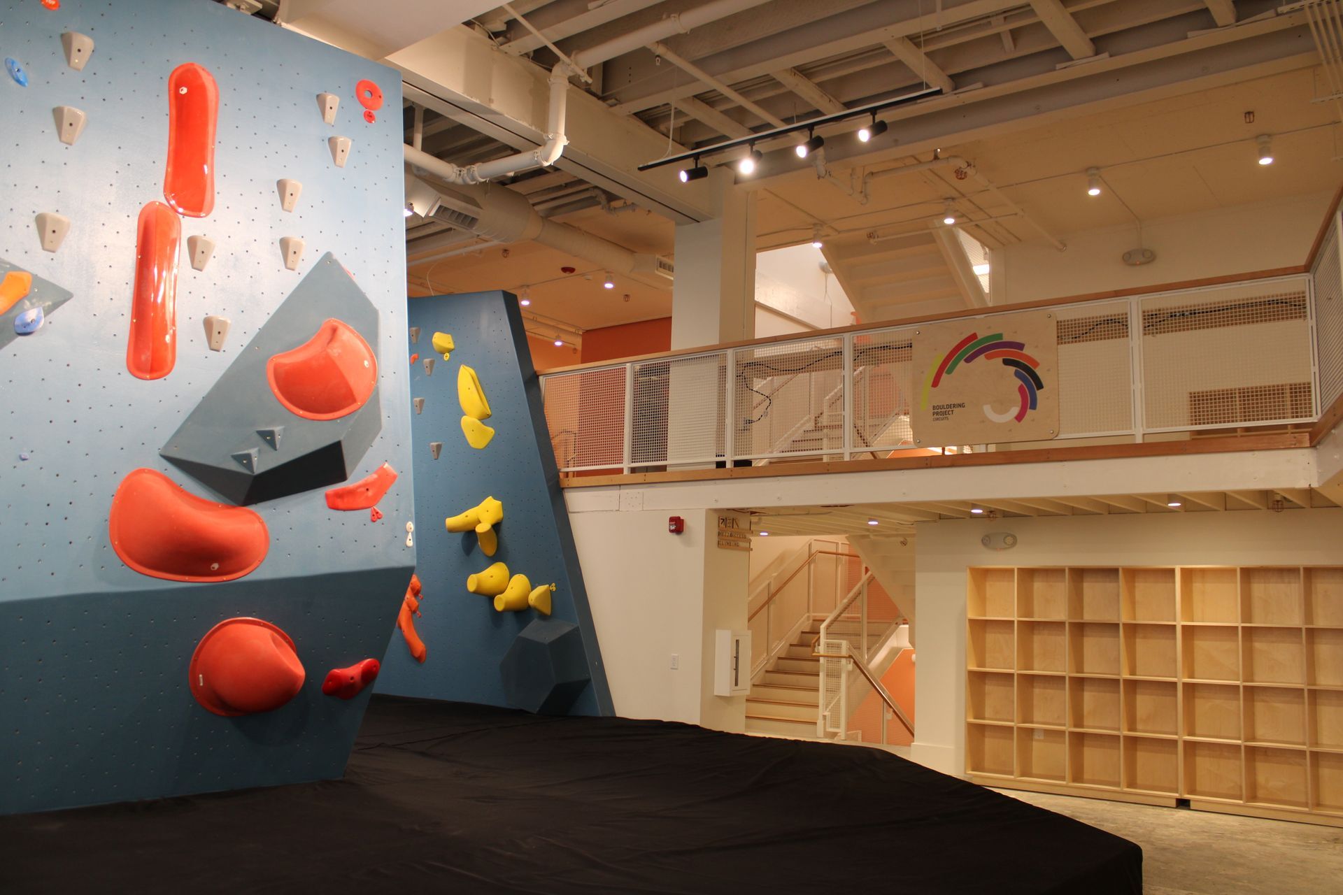 Indoor rock climbing gym with colorful walls, holds, and a second-story viewing area.