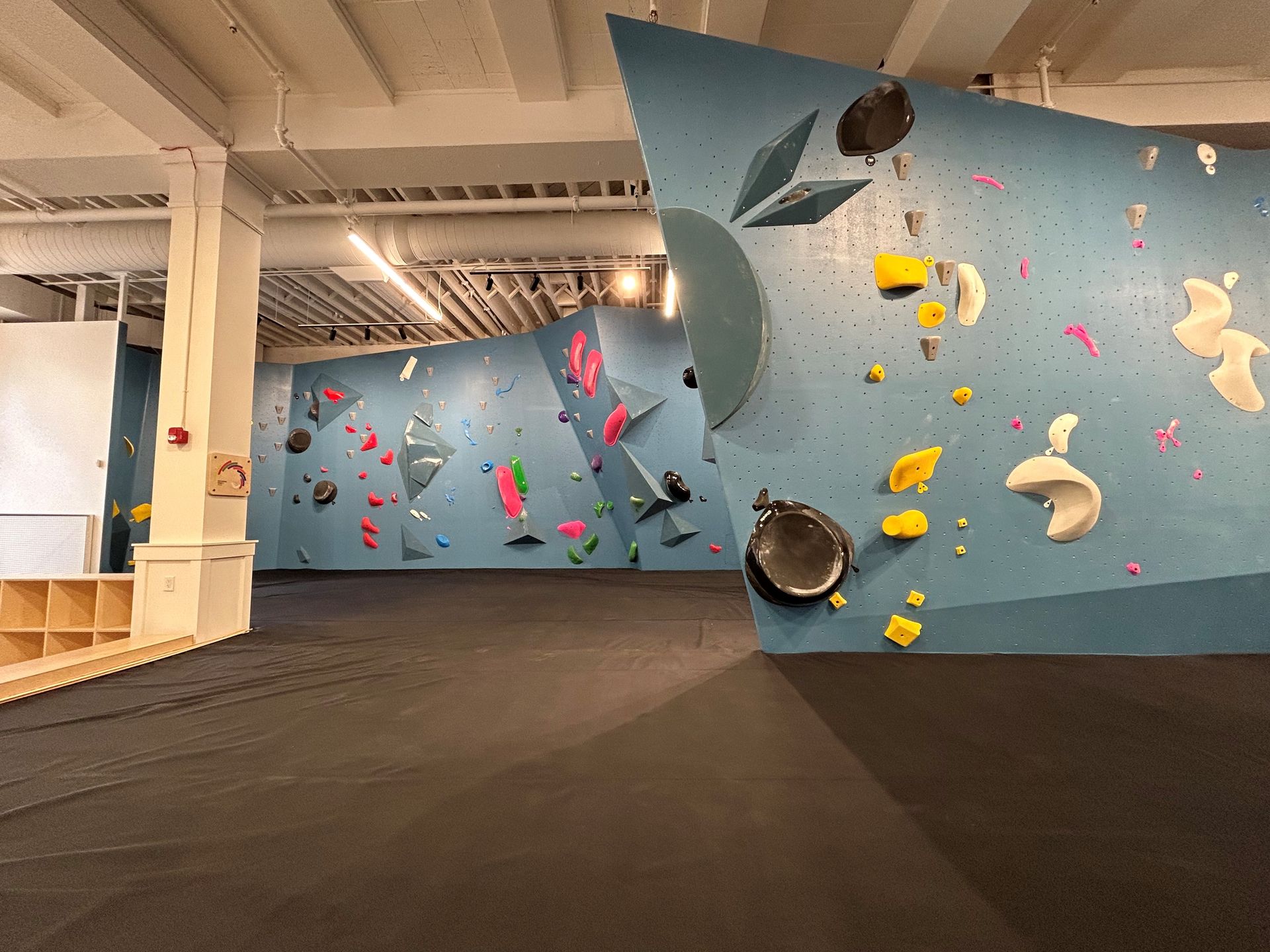 Indoor climbing gym with blue walls, colorful handholds, and black floor.