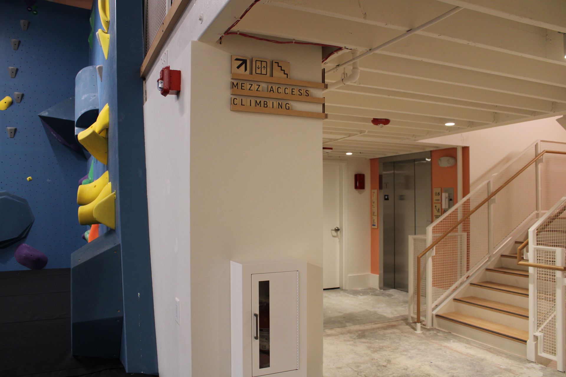 Entrance with a climbing wall, stairs, and elevator. Signage directs to areas.